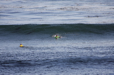 The surfer is waiting in a troth, the valley between the level water and the crest of the wave building behind him.