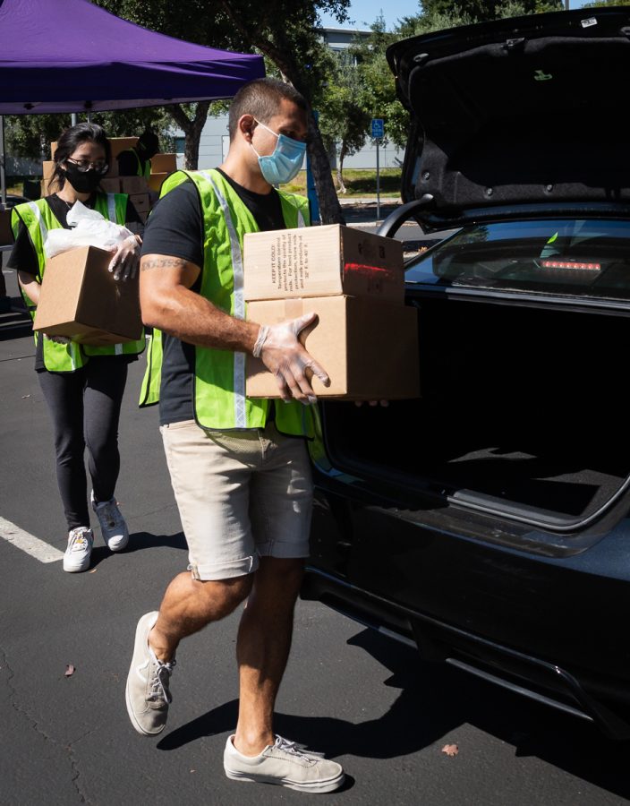 From left, San Jose State University student Tu Le, nutrition major, and SJCC transfer student Donovan Bedar, communications major, 26, load a waiting car with boxes of food at the San Jose City College campus grocery giveaway on July 8. 